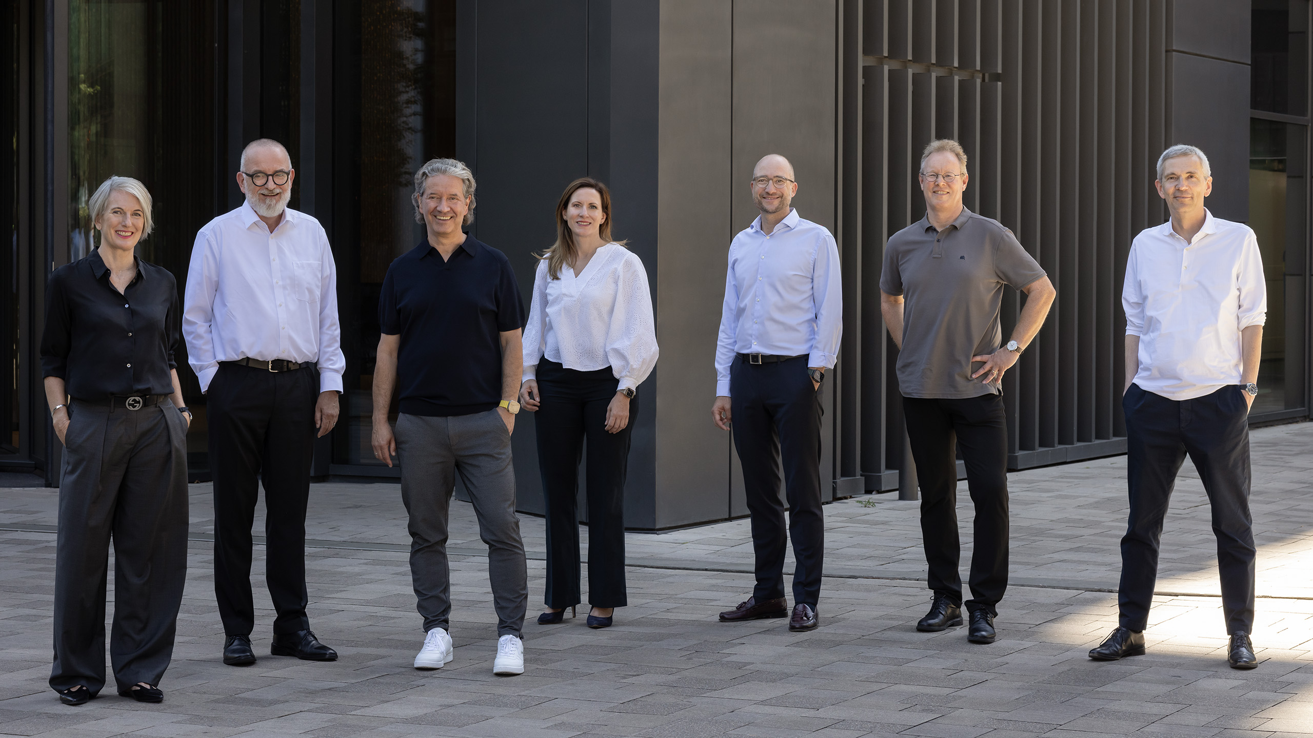 Teamfoto: Sieben Personen des Investment-Teams "KMU" vor einem modernen, dunklen Bürogebäude.