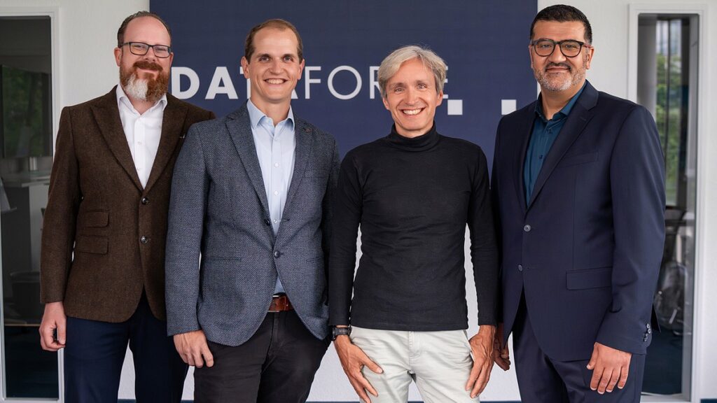 Gruppenaufnahme der Geschäftsführung von „Dataforce“: vier lächelnde Männer in legerer Business-Kleidung stehen nebeneinander vor einer blauen Wand mit dem Firmenschriftzug.