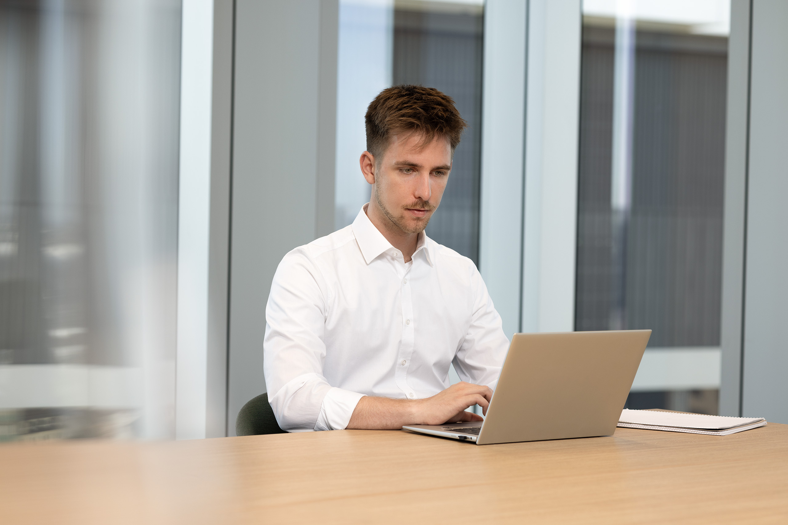Ein Mitarbeiter arbeitet konzentriert in einem hellen Büroraum an einem Laptop.